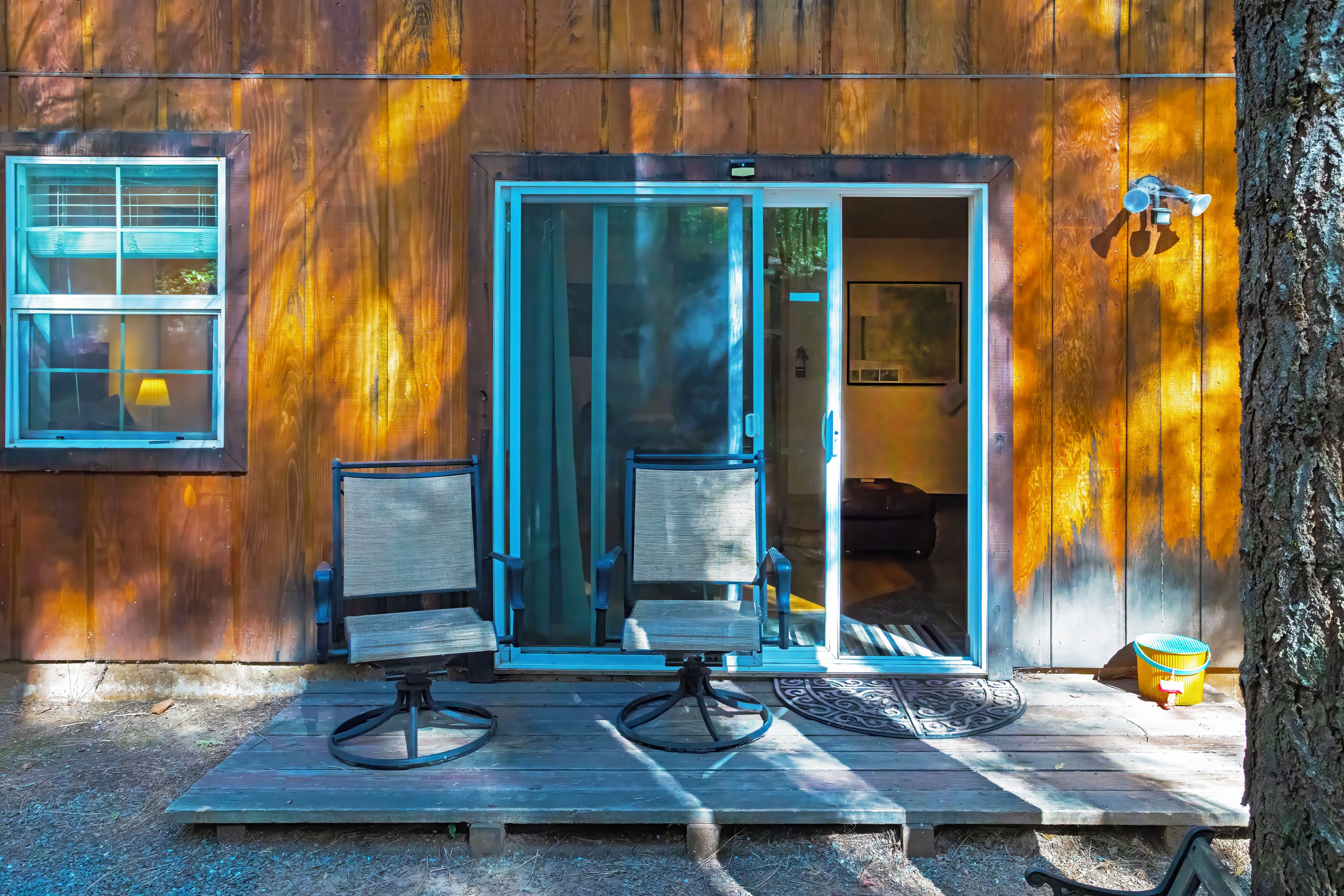 A wooden cabin with a sliding glass door, two chairs, and a small table.