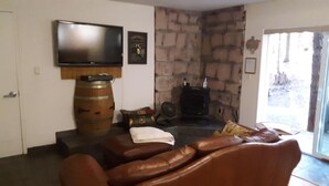 Ein Wohnzimmer mit Fernseher, Steinwand, Kamin, Ledersofa und einer zur Außenseite führenden Tür.