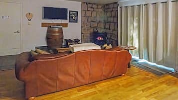A living room with a brown sofa, a television mounted on the wall, a stone wall, and a window with curtains.