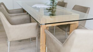 Una mesa de comedor moderna con tapa de vidrio y estructura de madera, rodeada por cuatro sillas color beige con patas de metal.