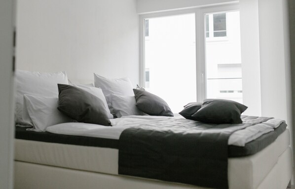 A bed with white and gray bedding, a black throw blanket, and a window with a view of buildings.