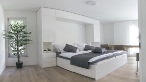 Un dormitorio moderno con una cama curvada, muebles blancos, una pequeña planta en maceta y un escritorio con silla.