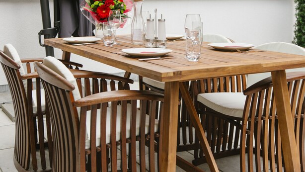 Una mesa de comedor de madera dispuesta con platos, vasos y un jarrón de flores.