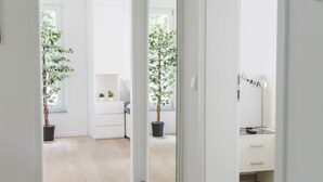 Un pasillo con suelo de madera que conduce a una habitación con un aparador blanco y una planta en maceta.
