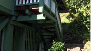 A green wooden building with a balcony and a stone staircase leading up to it.