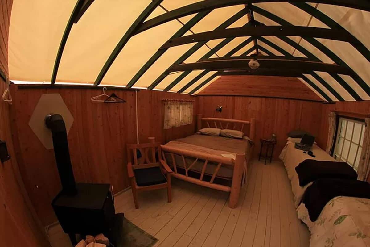 Een gezellig houten chalet met een bed, een stoel, een klein tafeltje en een open haard.