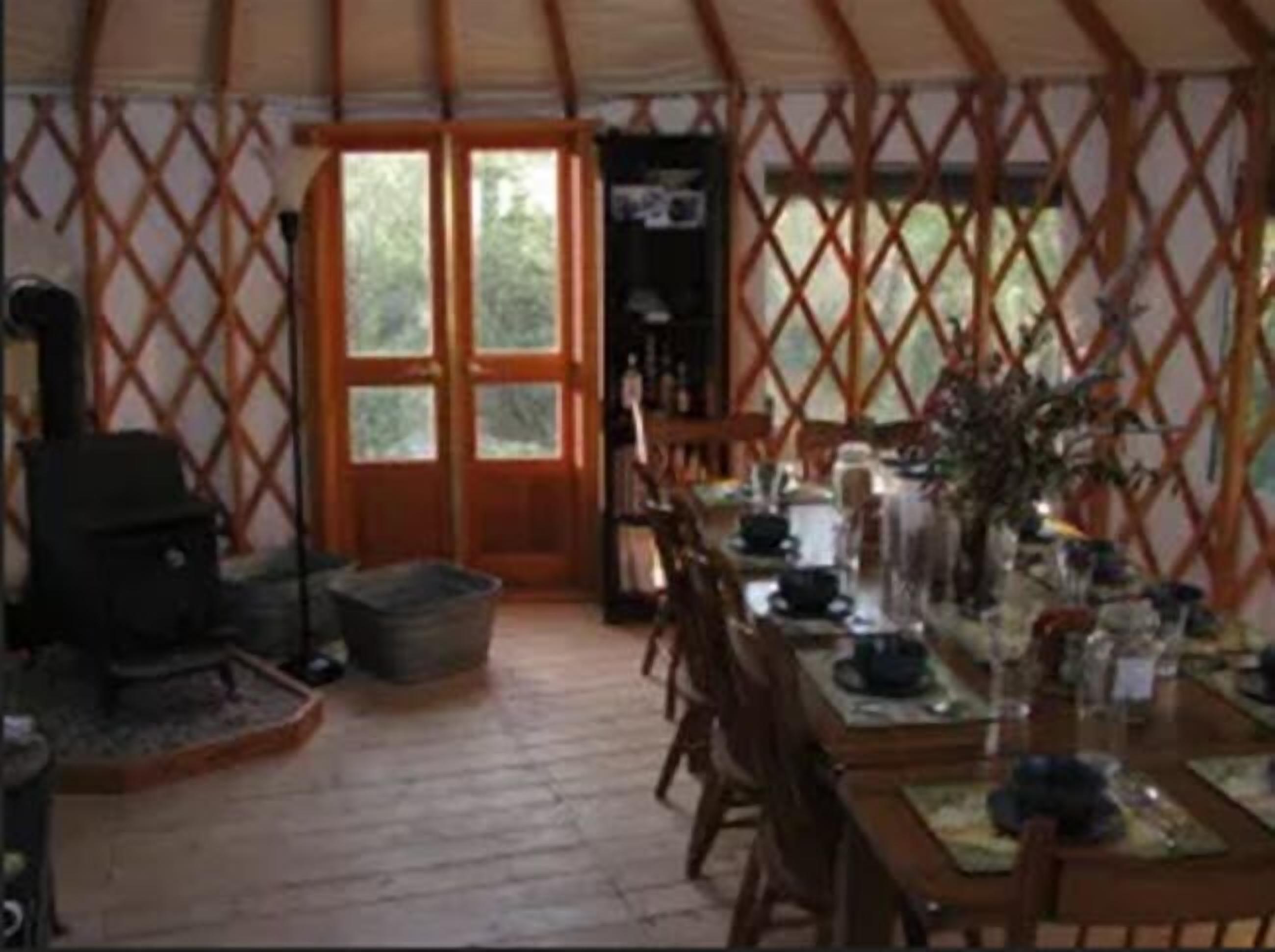 A yurt interior with a dining table set for four, a fireplace, and a large window.