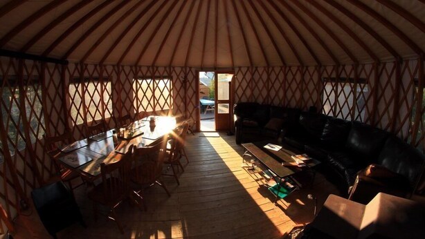 Interior de una yurta con una mesa de comedor central, un sofá y suelo de madera.