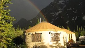 Una yurta con montañas al fondo y un arcoíris.
