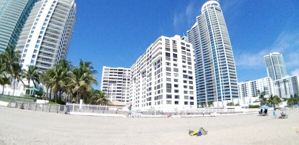Un hotel frente a la playa con varios edificios altos, palmeras y una playa de arena.
