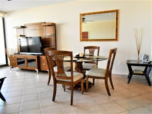 Un comedor con una mesa de madera, sillas, un televisor sobre un mueble de madera y un espejo en la pared.