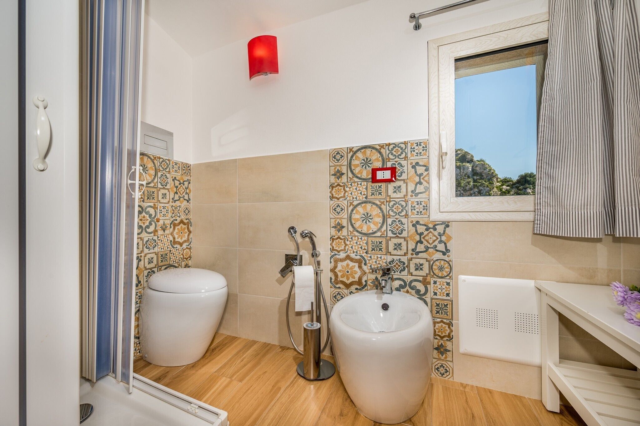 A bathroom with two toilets, a bidet, a sink, and a window with a view of the outdoors.
