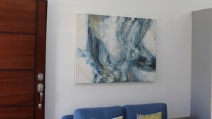 Ein modernes Wohnzimmer mit einem blauen Sofa, zwei Kissen, einer Holztür und einem großen abstrakten Gemälde an der Wand.