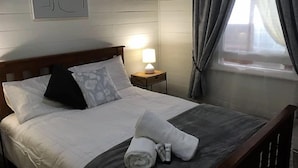 Un lit bien fait, avec des draps blancs, un oreiller et une serviette enroulée, posés sur une tête de lit sombre.