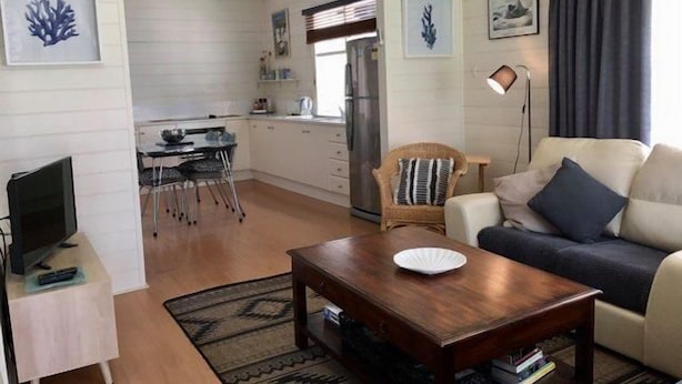 Un espace de vie compact comprenant un coin cuisine, un coin repas et un coin salon avec un canapé et un fauteuil.