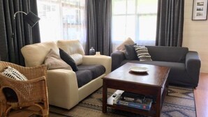 Un salon avec un canapé beige, un canapé gris foncé, une table basse en bois et un fauteuil en osier.