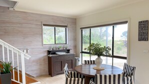 Una cocina moderna con comedor, que presenta una pared de madera, ventanas amplias y una mesa de comedor con sillas a rayas.
