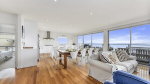 A modern living room with a dining area and a kitchen. There is a large window with a view of the sea. - Bayview - Fantastic Panoramic Views of Guichen Bay - Pet Friendly Inside (Robe)
