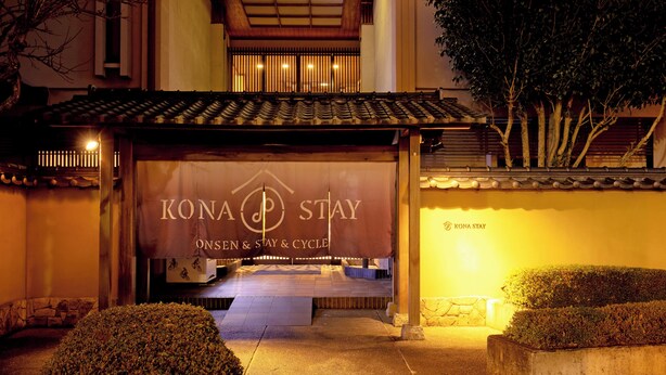 Entrada de hotel con un letrero que dice "KONA STAY" y un área cubierta con escalones que conducen a la entrada.