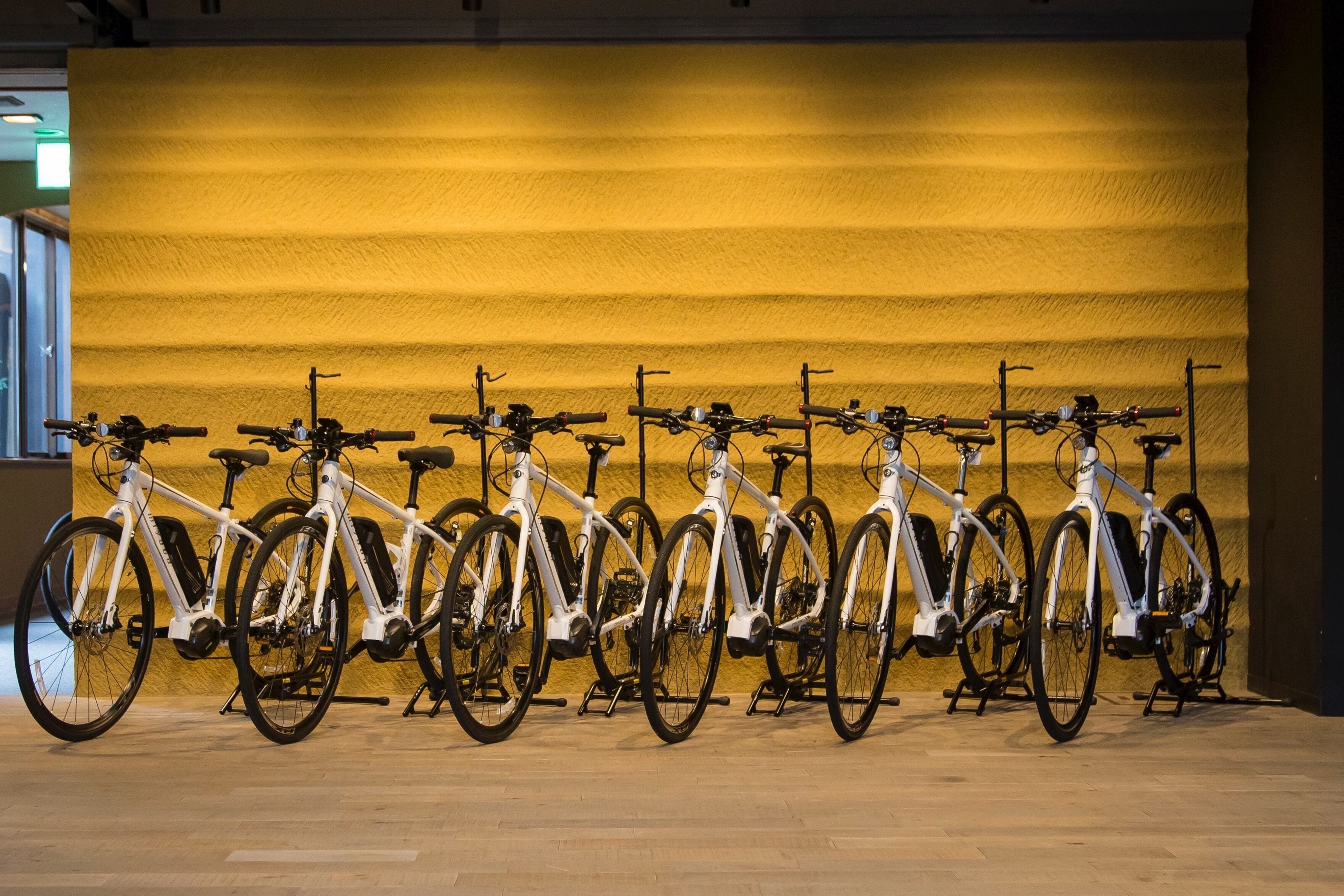 Una hilera de bicicletas blancas estacionadas frente a un muro amarillo.