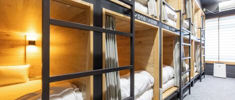 Habitación de hotel con literas, cabeceros de madera y una mesita de noche pequeña con lámpara.
