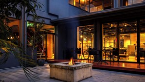 Un patio con un brasero, asientos al aire libre y la entrada de un edificio con puertas de vidrio.