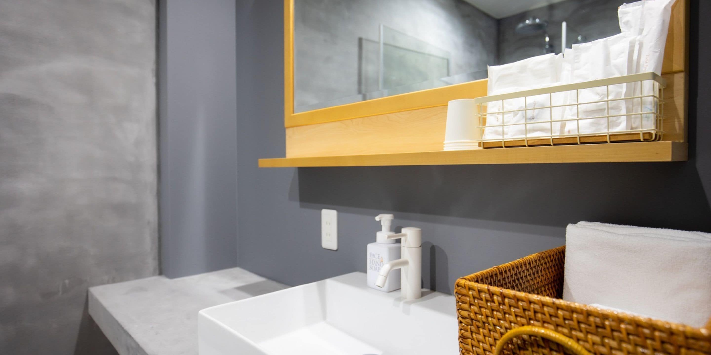 A bathroom with a white sink, a mirror above it, a wooden shelf with toiletries, and a wicker basket with a towel.