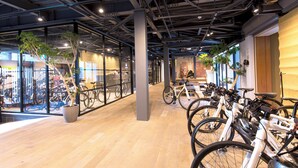 Un espacio interior moderno con suelo de madera, paredes de vidrio y un techo con vigas a la vista. Hay bicicletas estacionadas contra las paredes, y se ve una planta en maceta.