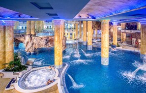 Una piscina interior con múltiples fuentes, columnas de piedra y un paisaje rocoso de fondo.