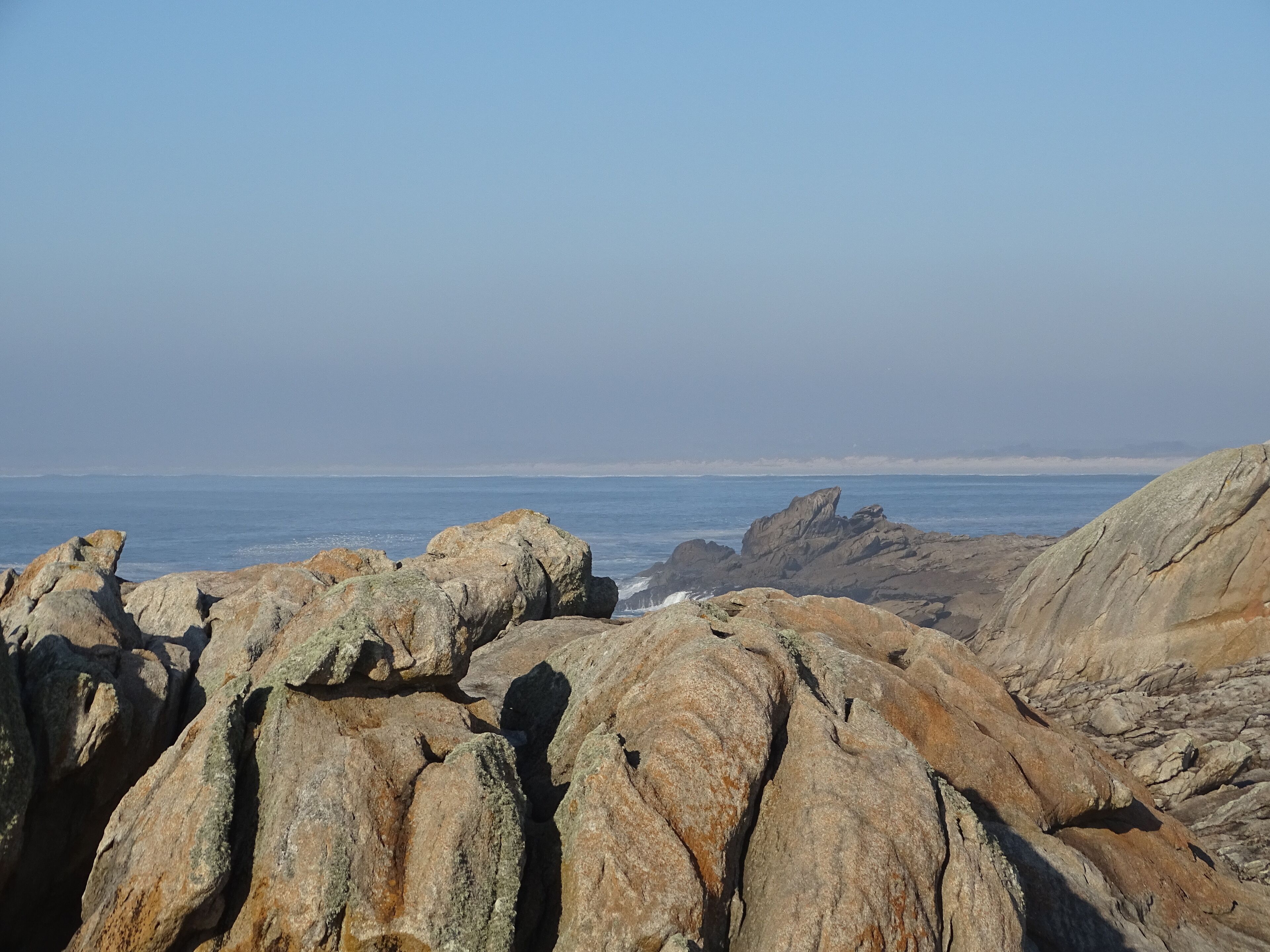 Eine felsige Küstenlinie mit großen Felsen und dem Meer im Hintergrund.