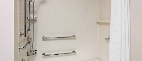A bathroom with a white bathtub, chrome fixtures, and grab bars.