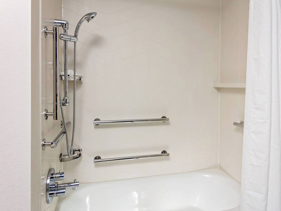 A bathroom with a white bathtub, chrome fixtures, and grab bars.