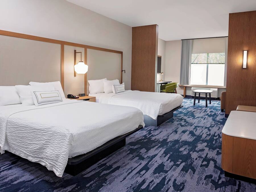 A hotel room with two beds, a desk, a chair, and a TV.