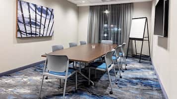 A conference room with a wooden table, six chairs, a whiteboard stand, and a large abstract painting on the wall.