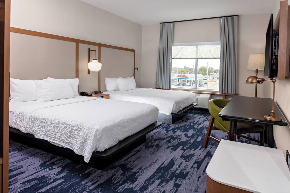 A hotel room with two beds, a desk, a chair, a TV, and a window with curtains.