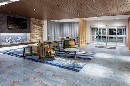 A lobby with a stone wall, a flat-screen TV, a reception desk, and a seating area with chairs and a sofa.