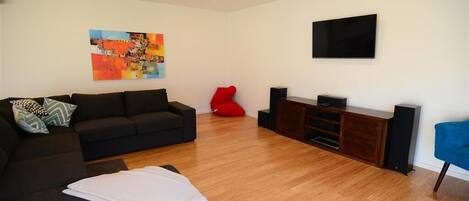 Una sala de estar con un sofá negro, un sillón de peluche rojo, un televisor de pantalla plana y un aparador de madera.