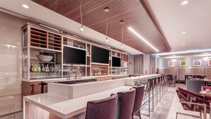 A modern bar area with a long counter, multiple seating options, and a variety of bottles and glasses. - Hilton Garden Inn Toronto Brampton West (Brampton)