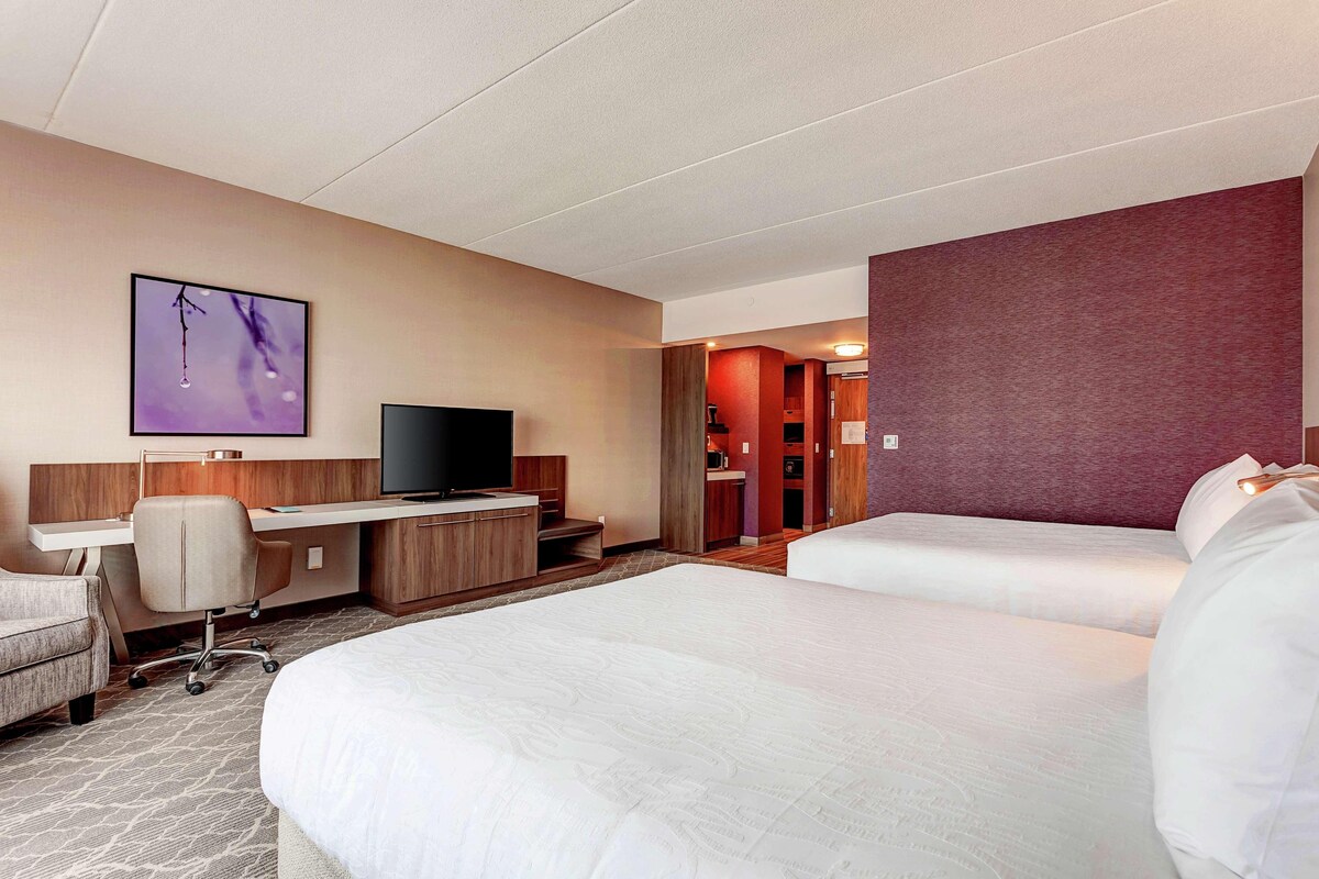 A hotel room with two beds, a desk, a chair, a television, and a bathroom visible through an open door.