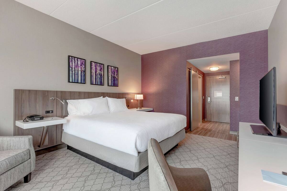 Une chambre d’hôtel avec un grand lit, un bureau avec une lampe, une télévision et des œuvres d’art accrochées au mur.