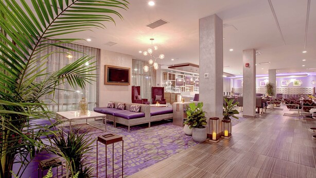A modern hotel lobby with a seating area, large windows, and decorative plants. - Hilton Garden Inn Toronto Brampton West (Brampton)
