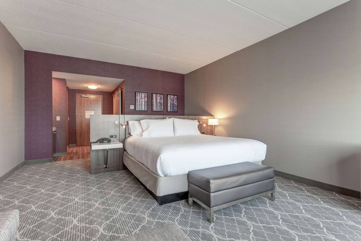 Une chambre d’hôtel avec un grand lit, une table de chevet, un banc et une lampe fixée au mur.