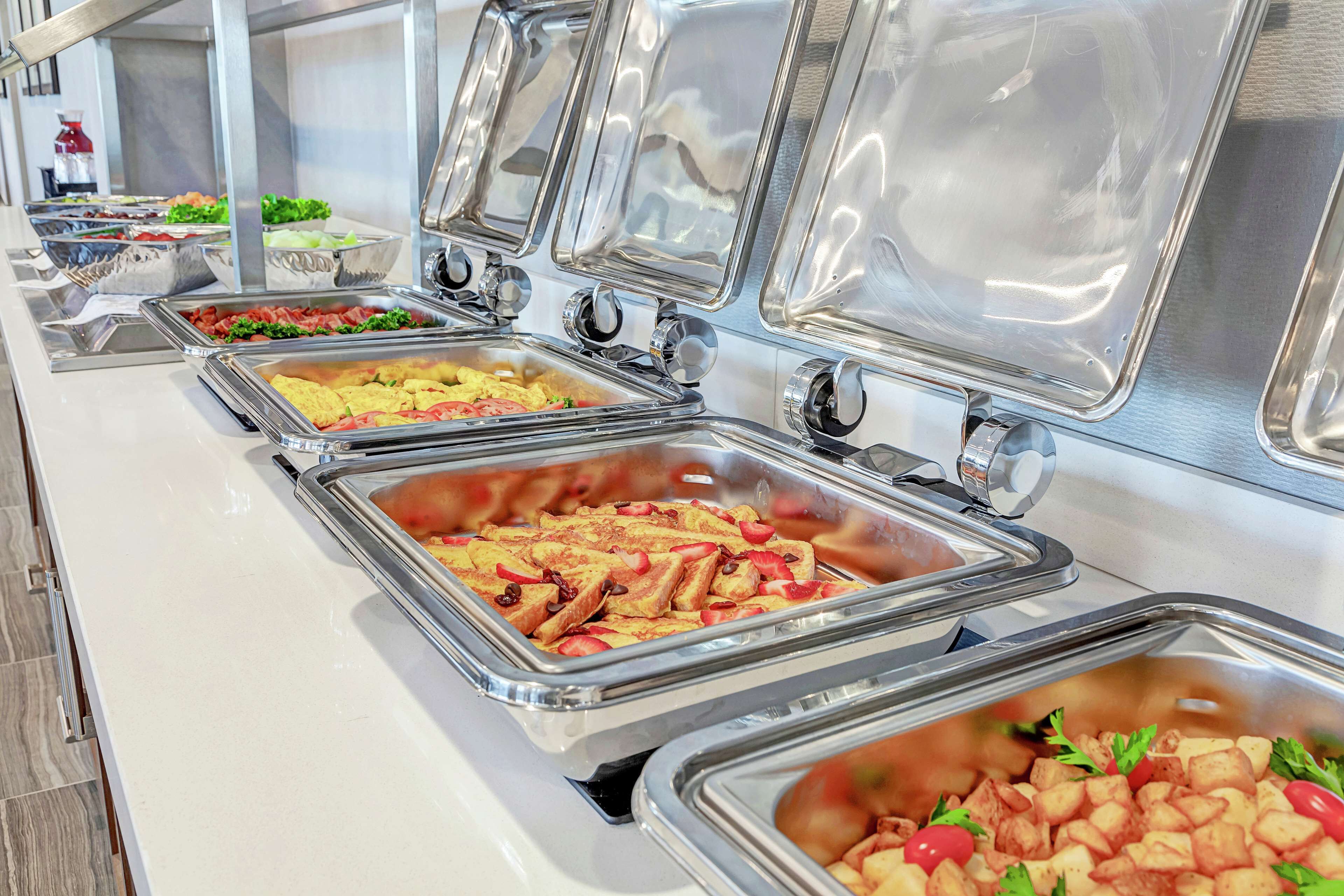 A buffet with various food items in metal containers, including salads, fruits, and other dishes.