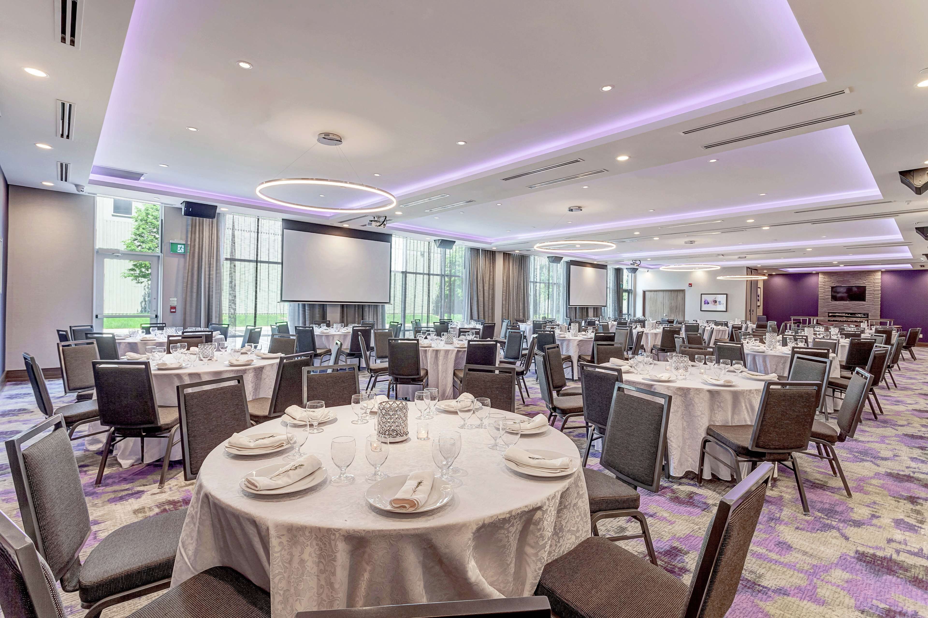 A large conference room with round tables set for dining, equipped with chairs and table settings.