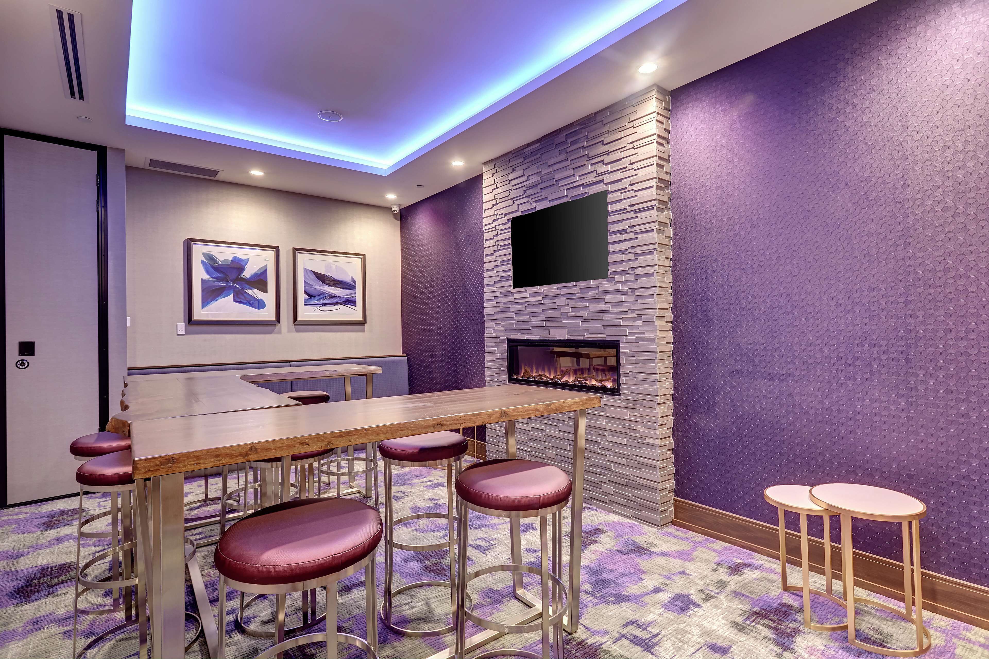 A modern bar area with a wooden table and bar stools, a flat-screen TV mounted on a textured wall, and a fireplace.