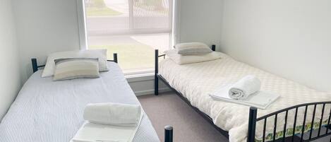 A small, clean room with two single beds, a window with a view of the outside, and a door.