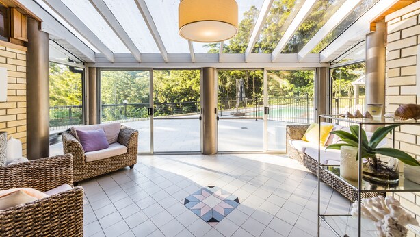 Amplo espaço interno com móveis de vime, uma mesa de centro de vidro e vista para o exterior.