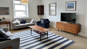 A living room with a sofa, armchair, coffee table, TV, and a cabinet. - Cornerstone Cottage - Historic 1850's Cottage Pets Welcome - Inside by neg (Robe)