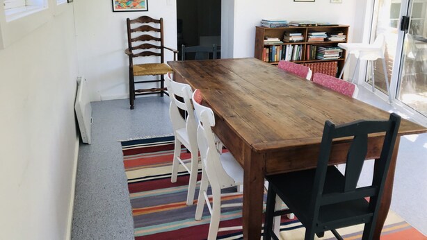 A dining area with a wooden table, white chairs, a colorful striped rug, and a bookshelf with books. - Cornerstone Cottage - Historic 1850's Cottage Pets Welcome - Inside by neg (Robe)