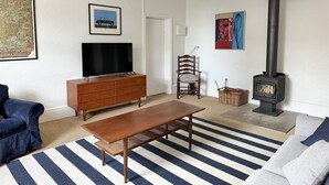 A living room with a television, wooden furniture, a bench, a sofa, a fireplace, and a map on the wall. - Cornerstone Cottage - Historic 1850's Cottage Pets Welcome - Inside by neg (Robe)